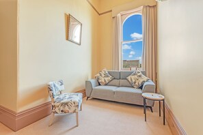 A living room with a sofa, armchair, and small table. - Clocktower Suites (Echuca)