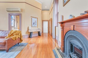 A spacious living room with a fireplace, a sofa, and a console table with a vase. - Clocktower Suites (Echuca)