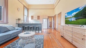 A modern living room with a grey sofa, a round coffee table, and a large TV on a wooden cabinet. - Clocktower Suites (Echuca)