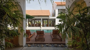Un espace aménagé au bord de la piscine, avec des chaises longues en bois et une vue sur une maison dont le toit est recouvert de tuiles.