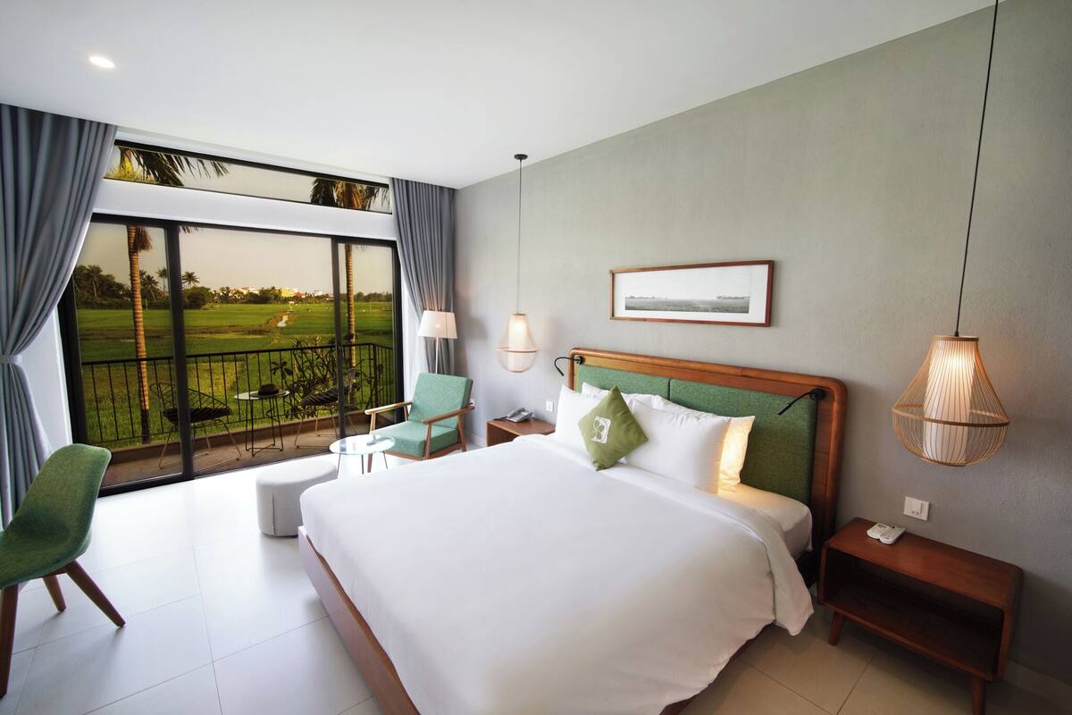 Ein Hotelzimmer mit einem großen Bett, Blick auf einen Golfplatz, einem Essbereich mit Stühlen und einem kleinen Tisch.