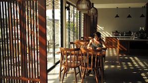 Un espace repas avec des chaises et des tables en bois, de grandes fenêtres et des lampes suspendues.