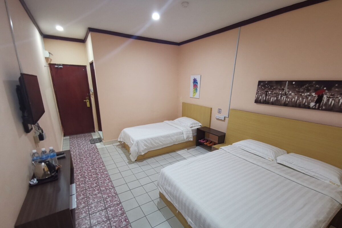 Une chambre d’hôtel avec deux lits, un bureau, une chaise, une télévision, une porte et un mur orné d’un tableau.