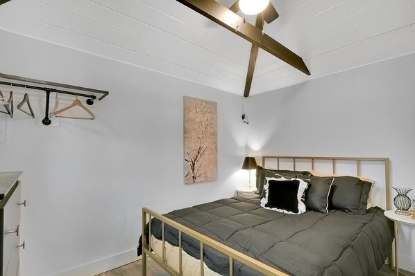 Ein Schlafzimmer mit Bett, Nachttisch, Lampe und einem an der Wand befestigten Kleiderhaken.