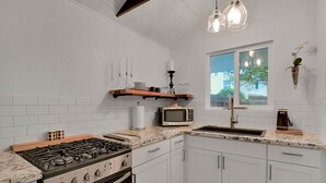 A modern kitchen with white cabinets, a gas stove, a microwave, and a sink. There is a window with a view of the outside.