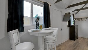A room with a round white table, two white chairs, a small potted plant, and a dark wooden cabinet.