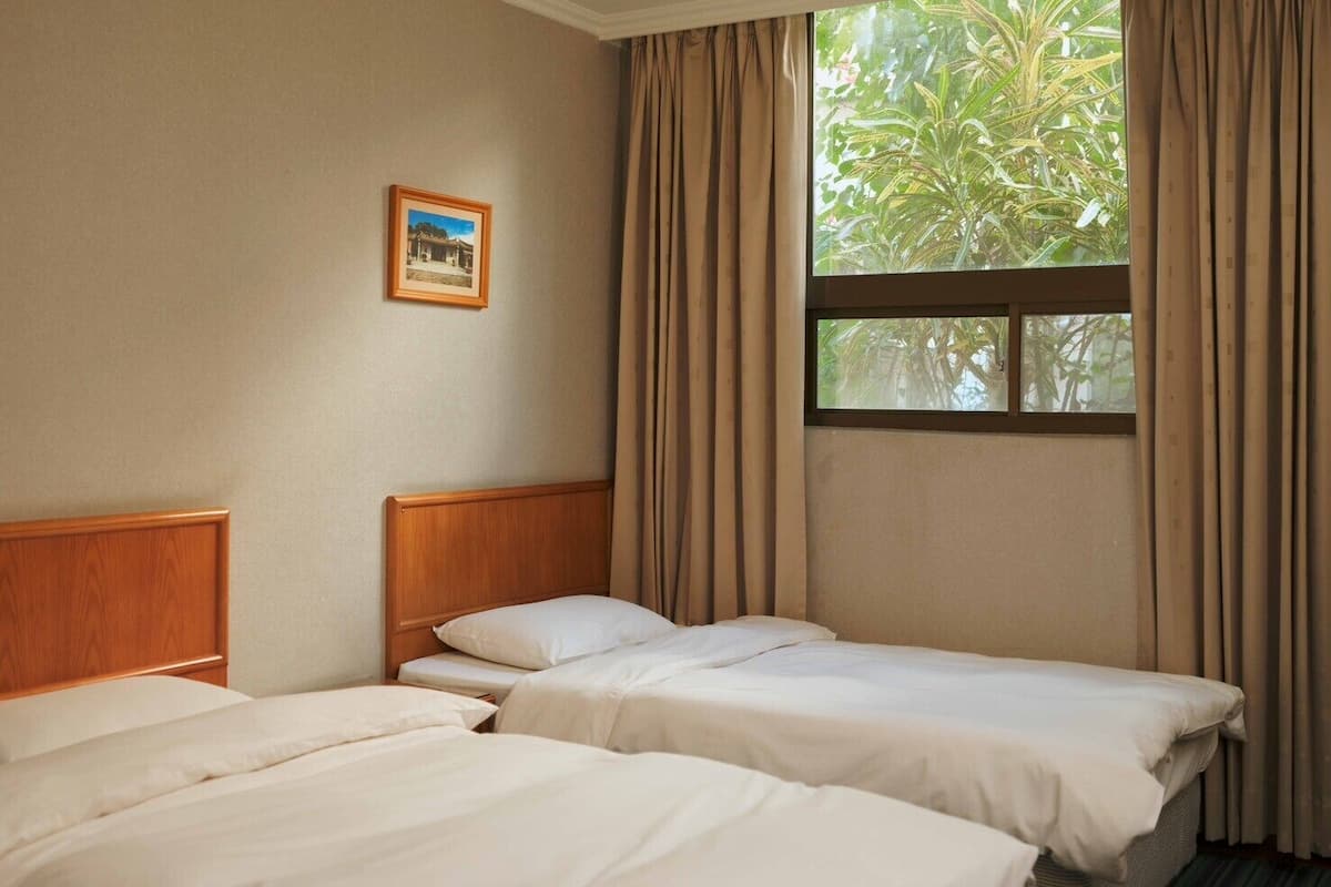 A hotel room with two single beds, a window with curtains, and a framed picture on the wall.