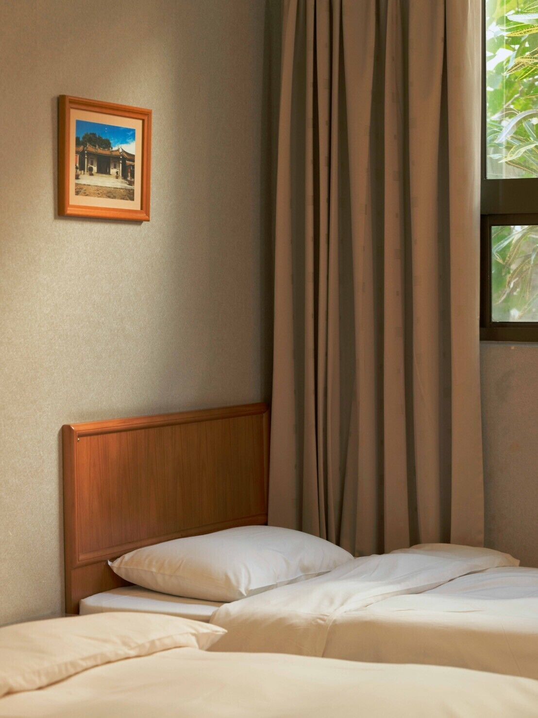 A bedroom with a wooden headboard, a bed with white bedding, a framed picture on the wall, and a window with curtains.