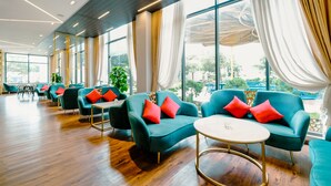 A modern hotel lobby with teal sofas, red cushions, and a wooden floor. - Sandals Star Hotel (Duc Trong)