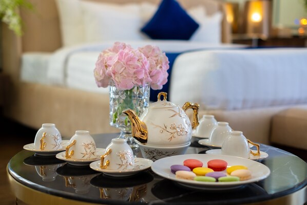Una mesa dispuesta con tazas y platillos blancos, una tetera dorada y un plato con macarons de colores.