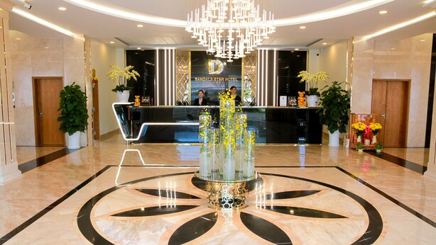 A hotel reception area with a modern design, featuring a central decorative fountain, a reception desk, and two potted plants. - Sandals Star Hotel (Duc Trong)