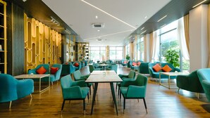 A spacious indoor area with multiple seating arrangements, including tables and chairs, and large windows providing natural light. - Sandals Star Hotel (Duc Trong)