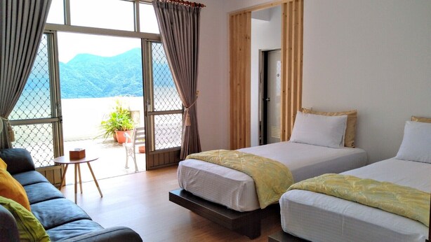 A hotel room with two beds, a sofa, and a small table. There is a balcony with a view of mountains. - Pu Su Bed and Breakfast (Lugu)