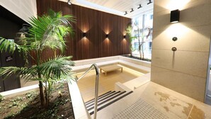A modern indoor relaxation area with a wooden wall, seating, and a small palm tree. - Melbourne CBD 2BD! - Experience Rose Lane! (Melbourne)