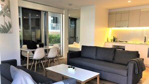 A modern living room with a grey sofa, white coffee table, and a dining area with a table and chairs. - Melbourne CBD 2BD! - Experience Rose Lane! (Melbourne)