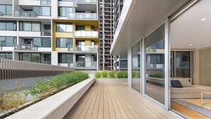 A modern apartment building with balconies, a wooden deck, and a glass door leading to a living area. - Melbourne CBD 2BD! - Experience Rose Lane! (Melbourne)