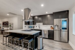 A modern kitchen with dark cabinetry, stainless steel appliances, and a central island with bar stools.