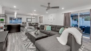 A modern living room with a grey sofa, coffee table, and a dining area with a chandelier. - OLD TOWN + HOME + HEATED Private POOL + 4 Bed/ 2.5 Bath + NEW Remodel+ Game Room (Scottsdale)