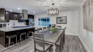 A modern kitchen with dark cabinetry, a central island with bar stools, a dining table with chairs, and a pendant light. - OLD TOWN + HOME + HEATED Private POOL + 4 Bed/ 2.5 Bath + NEW Remodel+ Game Room (Scottsdale)