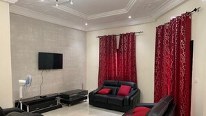 Ein modernes Wohnzimmer mit einem Flachbildfernseher, schwarzen Ledersofas mit roten Kissen, einem schwarzen Couchtisch und roten Vorhängen.