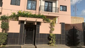 Ein zweistöckiges Gebäude mit Balkon, schwarzem Tor und kleinem Garten mit Pflanzen.