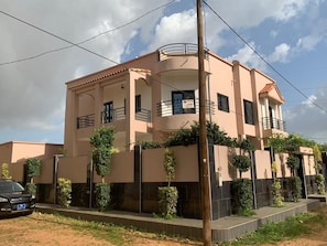 A two-story building with a balcony, a car parked in front, and a clear sky.