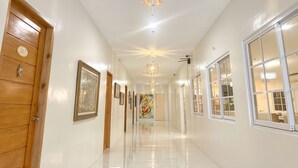 A hallway with wooden doors, framed artwork, and a chandelier. - Casa Bicolandia Suites (Daraga)