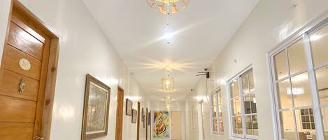 A hallway with wooden doors, framed artwork, and a chandelier.