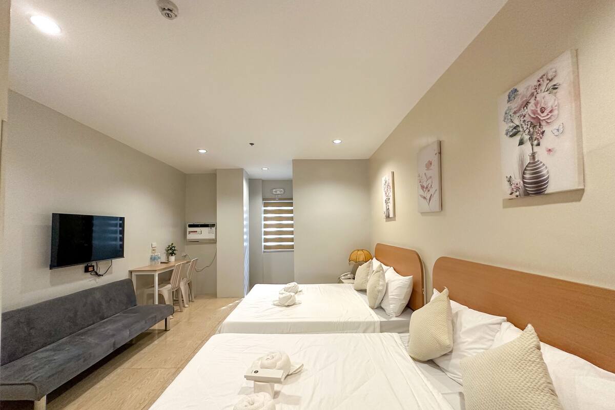 A hotel room with two beds, a sofa, a TV, and a small table with a lamp.