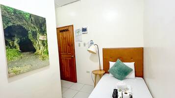 Habitación de hotel con cama, mesita de noche, lámpara, toma de corriente en la pared y una puerta.