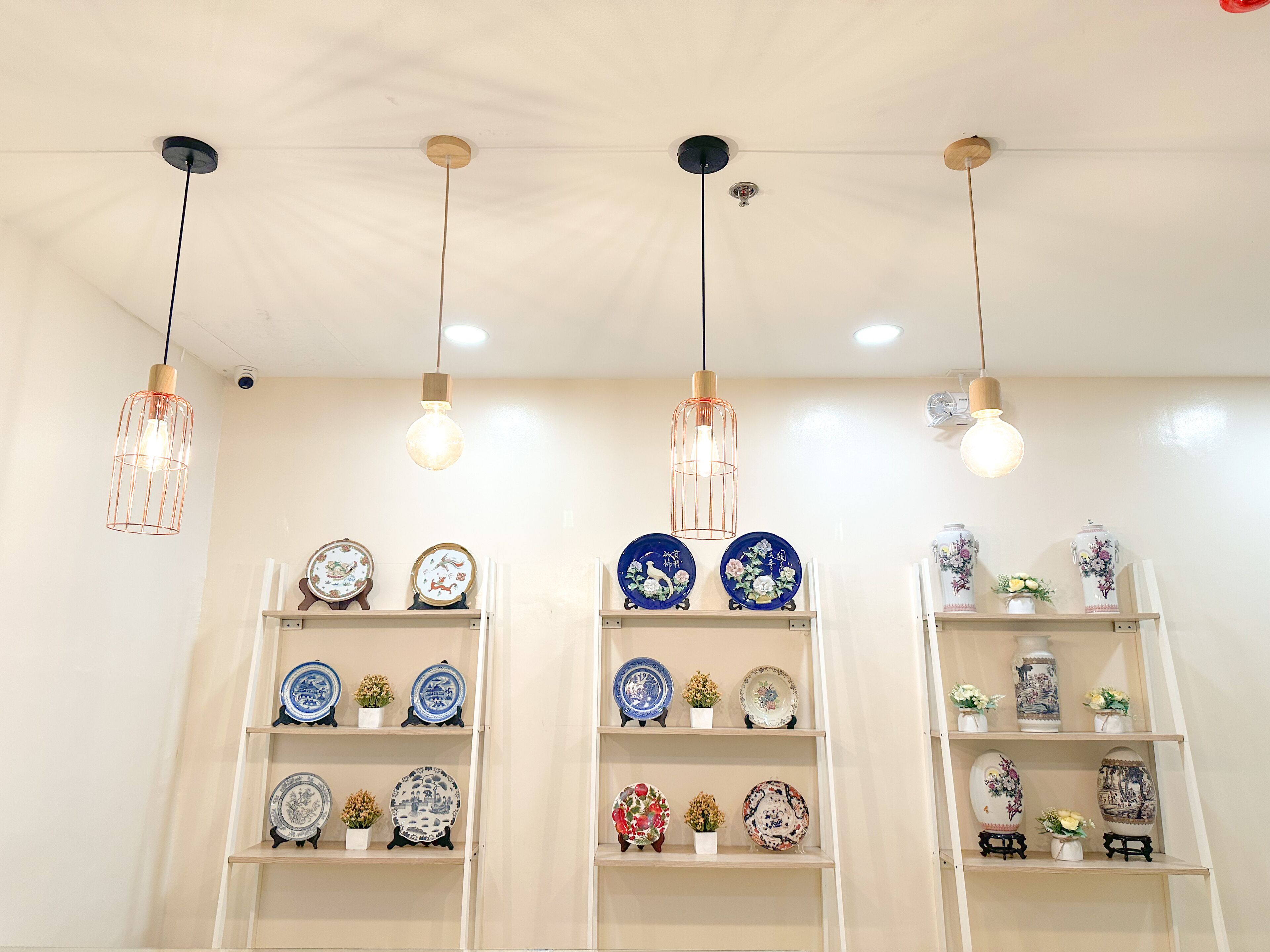 A room with multiple hanging pendant lights and shelves displaying ceramic plates and vases.
