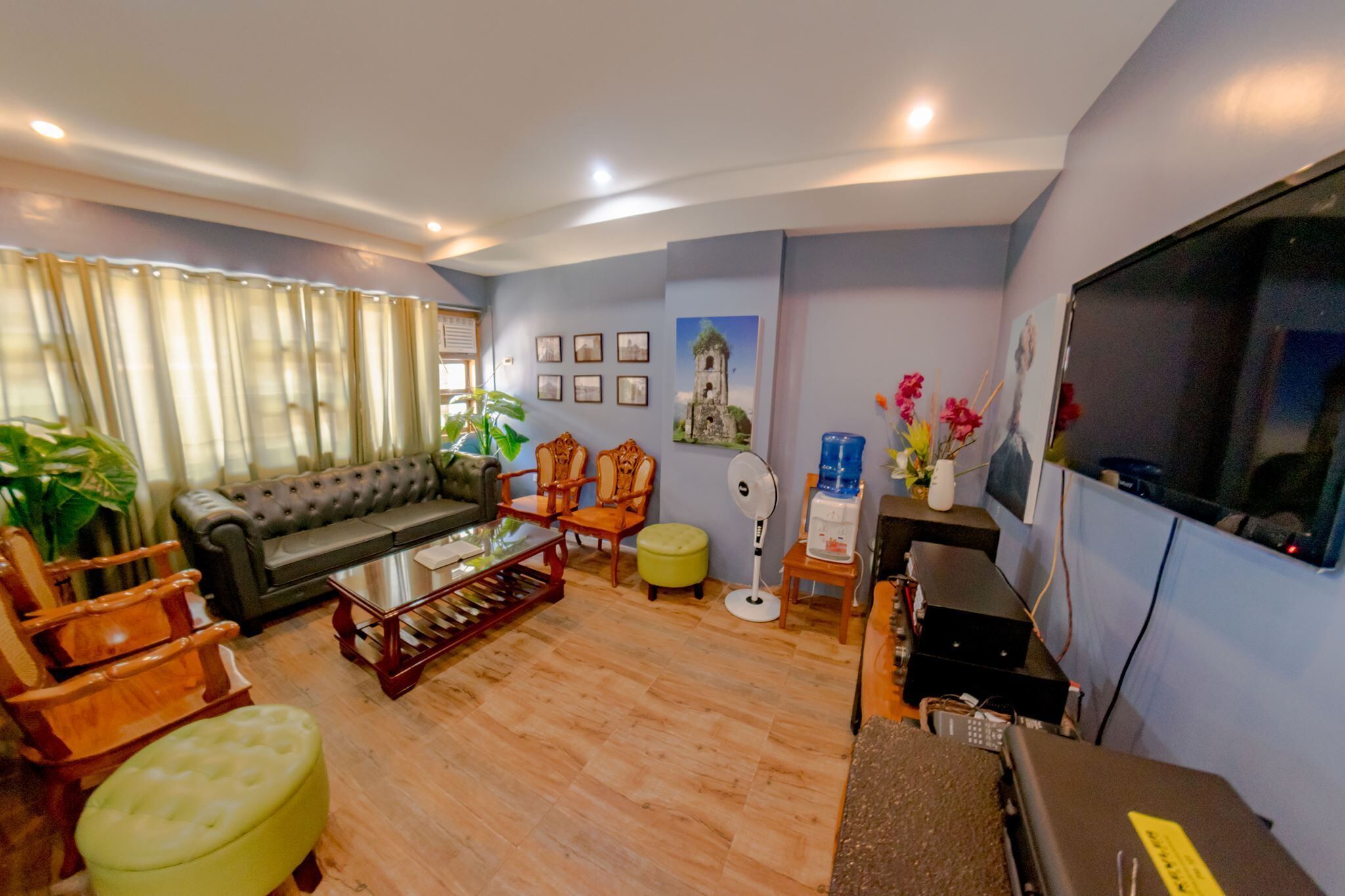 Una sala de estar con sofá, sillas, una mesa de centro, televisión y ventilador.