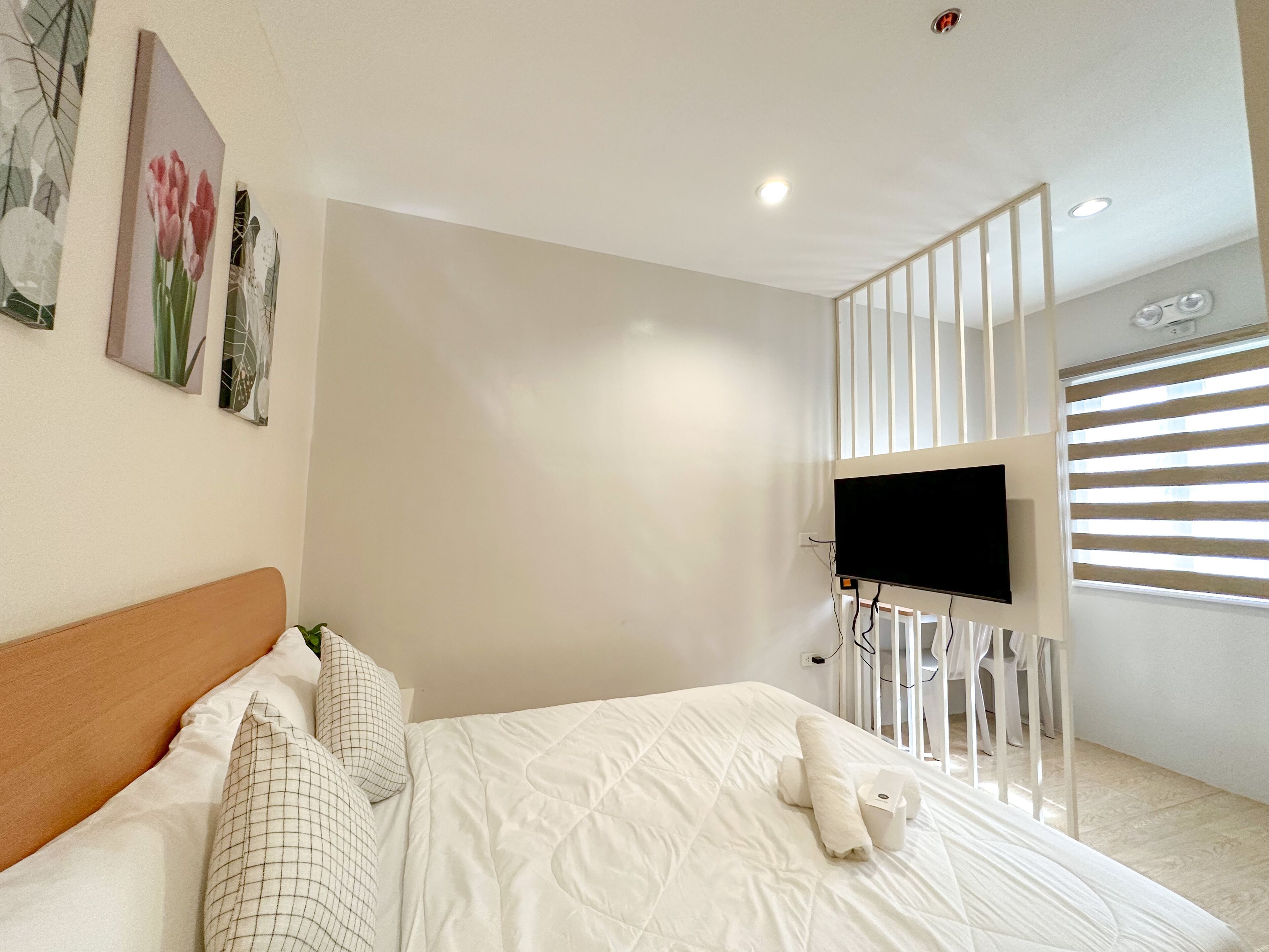 A bedroom with a bed, pillows, a TV mounted on a wall, and a window with blinds.