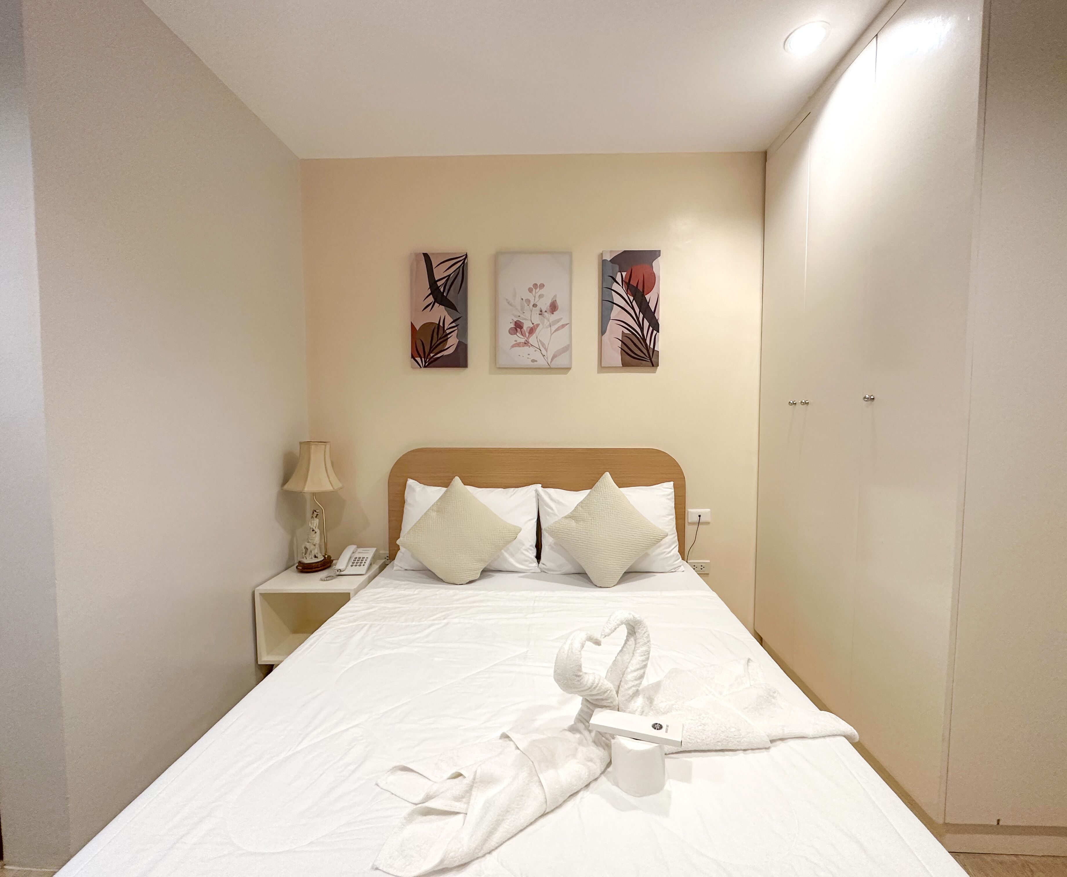 A hotel room with a bed, a nightstand with a lamp and phone, and artwork on the wall.