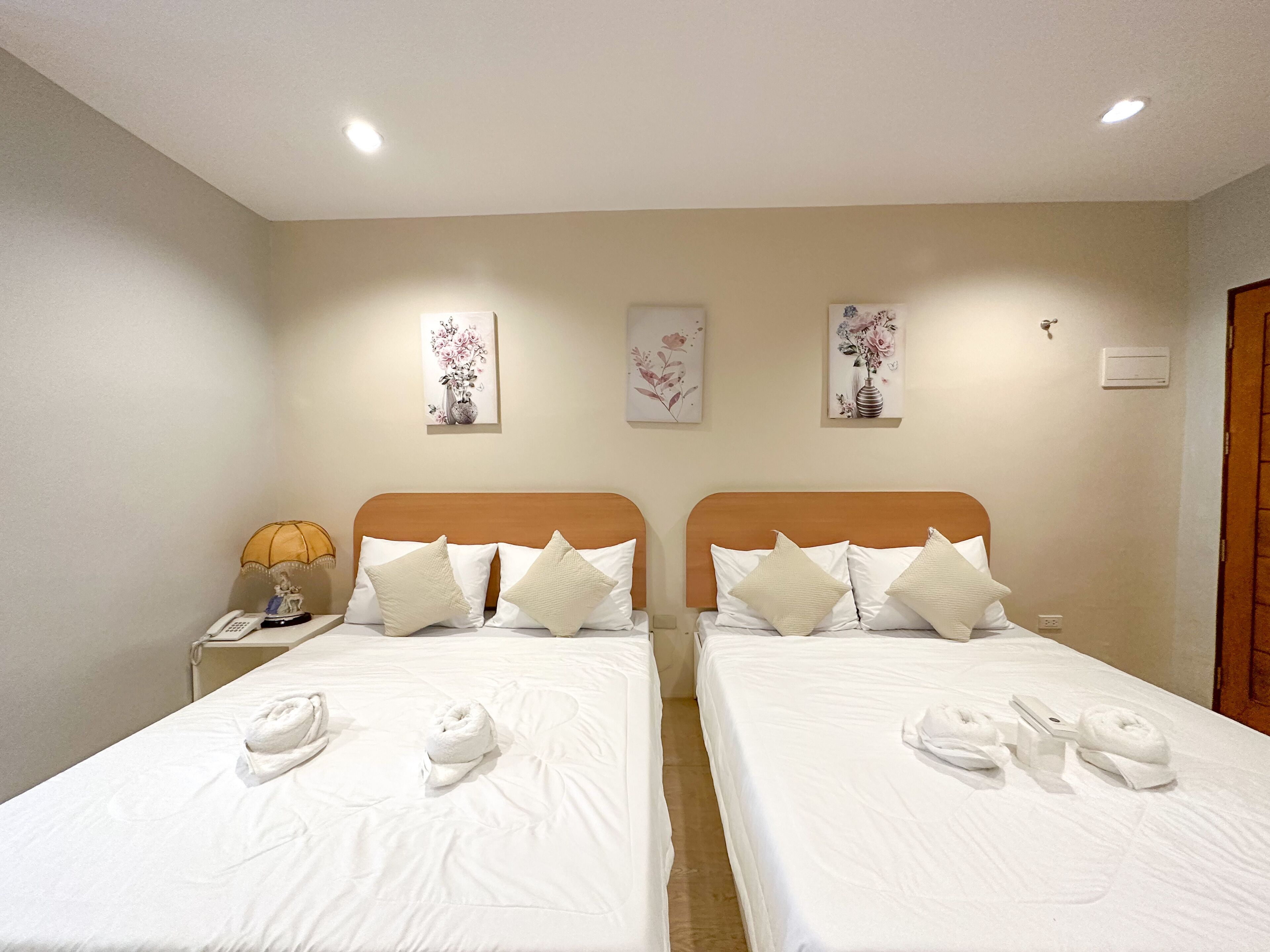 A hotel room with two beds, each with white linens and pillows, a nightstand with a lamp, and artwork on the walls.