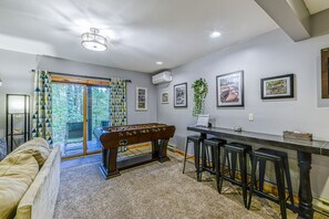 Una habitación con mesa de futbolín, taburetes de bar, sofá y vistas a través de un ventanal.