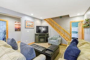 Una sala de estar con televisión, sofás, una mesa de centro, una escalera y una puerta que da a una cocina.