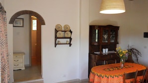 A dining area with a table covered in a patterned tablecloth, a vase with flowers, and a wooden cabinet with glass doors.