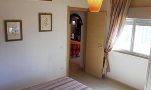 A bedroom with a bed, a wardrobe, a door leading to a hallway, and a window with curtains. - Casa Anselmi - Apartment in the countryside of Portoferraio (Portoferraio)