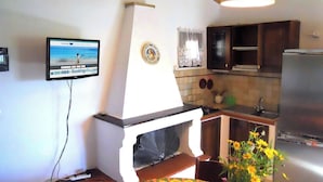 A kitchen with a built-in stove, a sink, and a refrigerator. There is a television mounted on the wall displaying a beach scene.