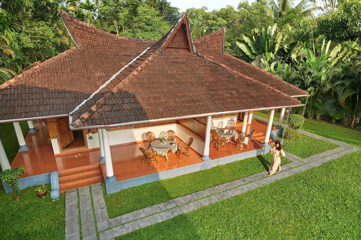 A traditional house with a tiled roof, a covered porch with furniture, and a well-maintained lawn.