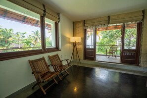 Una habitación con dos sillas de madera, una lámpara de pie y vistas a palmeras a través de amplios ventanales.