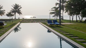 Piscina com espreguiçadeiras e palmeiras, com vista para um corpo d'água.