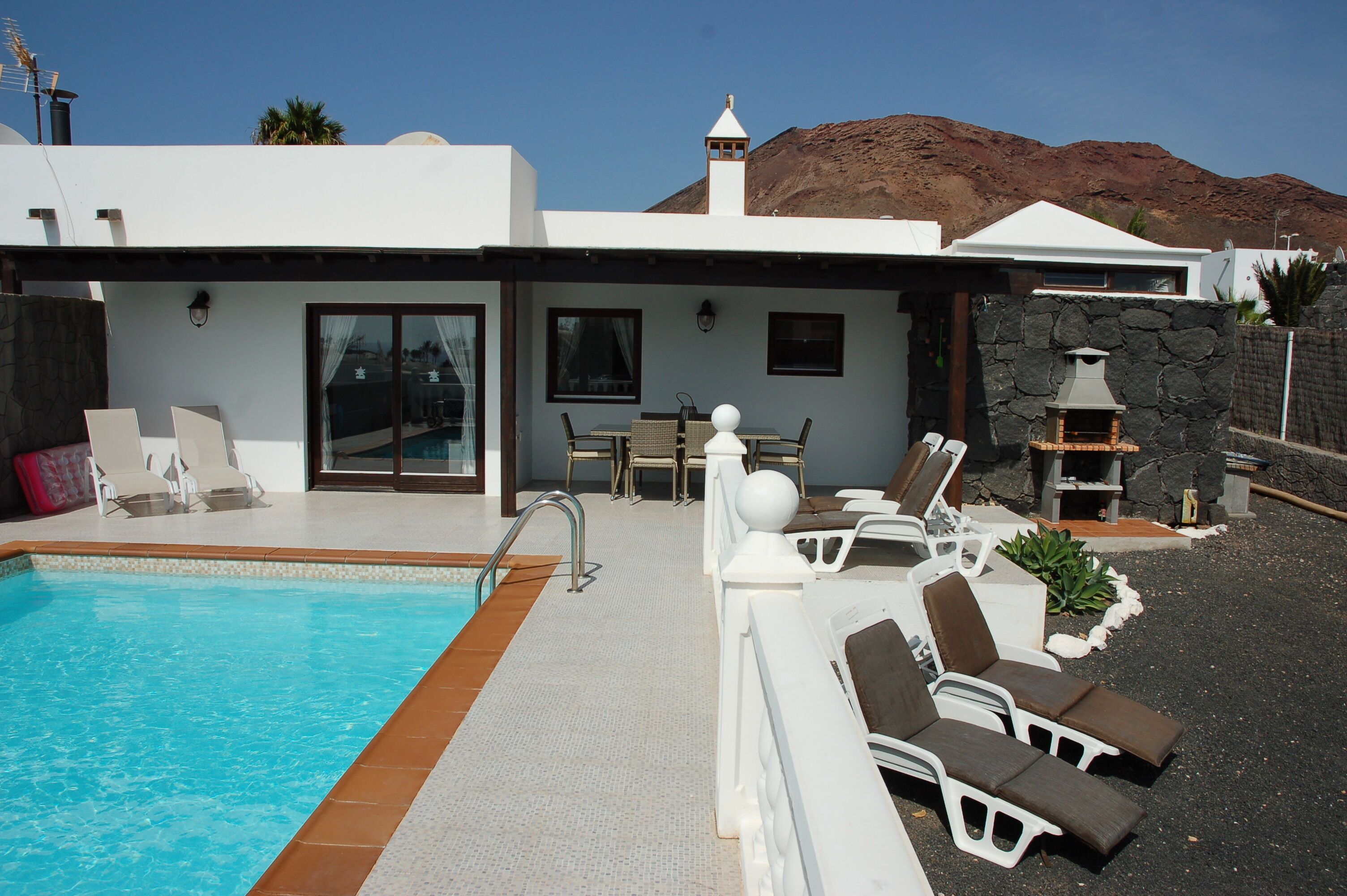 Eine moderne Villa mit Swimmingpool, Sitzgelegenheit im Freien und einem Kamin aus Stein.