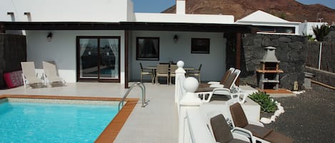A modern villa with a swimming pool, outdoor seating, and a stone fireplace.