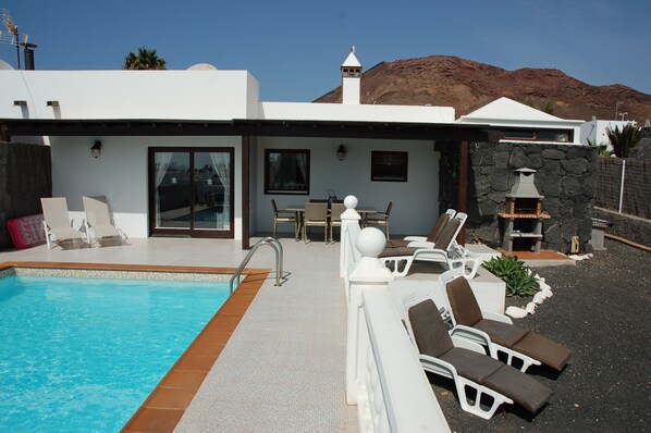 A modern villa with a swimming pool, outdoor seating, and a stone fireplace.