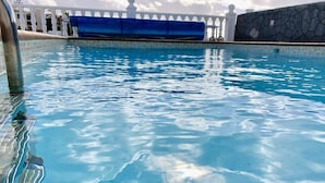 Ein klarer Pool mit weißem Geländer und einer Steinwand im Hintergrund.