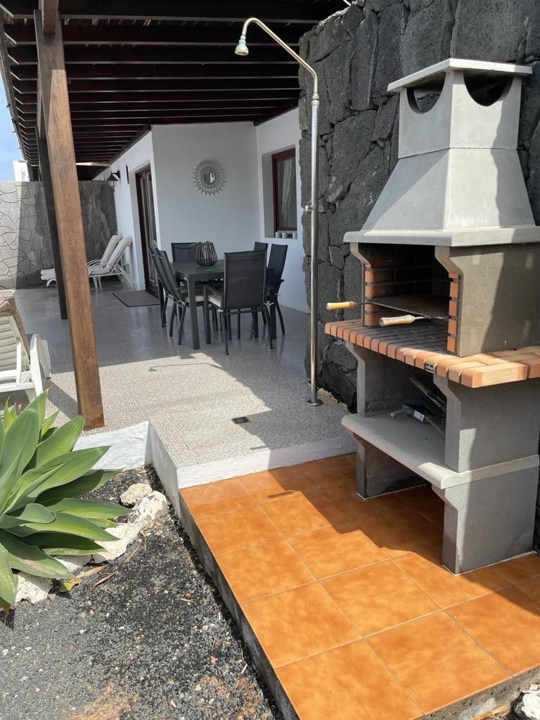 An outdoor patio with a stone wall, a barbecue grill, and a dining area with chairs and a table.