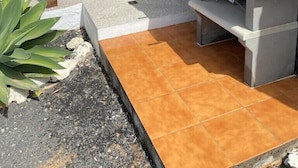 Eine Terrasse im Freien mit einer Steinmauer, einem Grill und einem Essbereich mit Stühlen und einem Tisch.