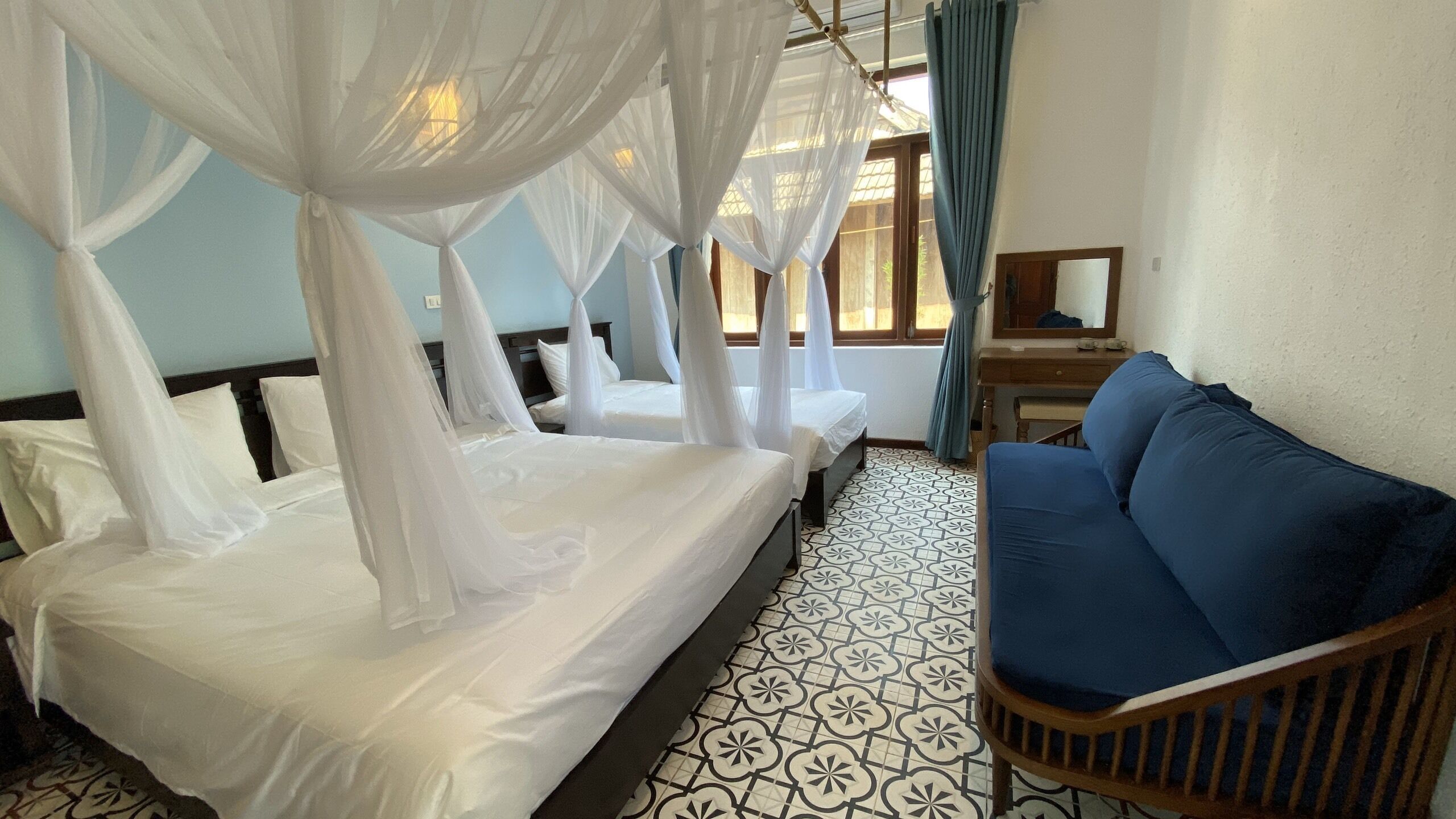 A hotel room with two beds covered in white bedsheets, a blue sofa, and a patterned floor.
